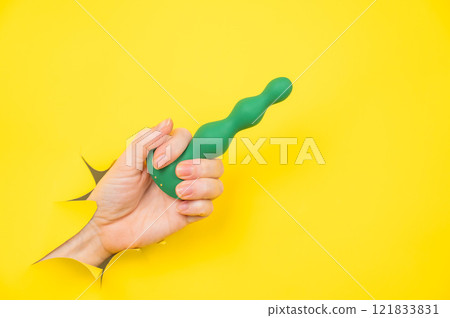 Female hand with green anal plug sticking out of yellow paper background. Copy space. Female hand with green anal plug sticking out of yellow paper background. Copy space. 121833831