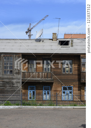 An old wooden house in Ulan-Ude, Russia, with a satellite antenna and a construction crane behind it An old wooden house in Ulan-Ude, Russia, with a satellite antenna and a construction crane behind it 121837312