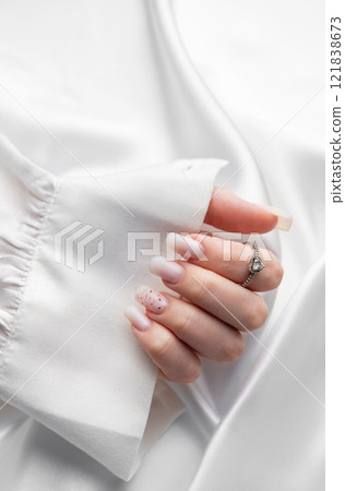 Woman showing stylish pastel pink manicure and silver ring on white silk fabric Woman showing stylish pastel pink manicure and silver ring on white silk fabric 121838673
