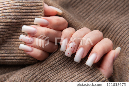 Woman showing stylish white manicure on brown knitted sweater Woman showing stylish white manicure on brown knitted sweater 121838675