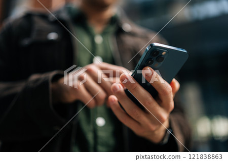 Close-up hands of unrecognizable man holding and using smartphone standing on city street, browsing internet, checking social media, using mobile application. Concept of modern communication. Close-up hands of unrecognizable man holding and using smartphone standing on city street, browsing internet, checking social media, using mobile application. Concept of modern communication. 121838863