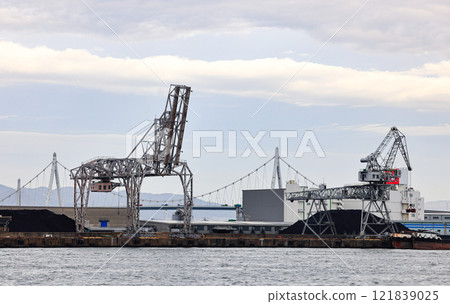 Large crane works on large coal stockpile and container at Industrial port. Cargo transportation and activity at modern shipping container terminal. Large crane works on large coal stockpile and container at Industrial port. Cargo transportation and activity at modern shipping container terminal. 121839025