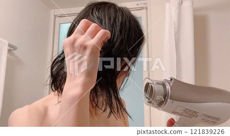 婦女用吹風機烘乾她的頭髮。 婦女用吹風機烘乾她的頭髮。 121839226