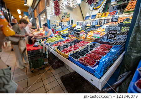 Budapest, Hungary. August 29,2022. The covered market, detail of a fruit vendor's stall. In the foreground, brightly colored berries. In the blurred background, a customer pays the vendor. Budapest, Hungary. August 29,2022. The covered market, detail of a fruit vendor's stall. In the foreground, brightly colored berries. In the blurred background, a customer pays the vendor. 121840079