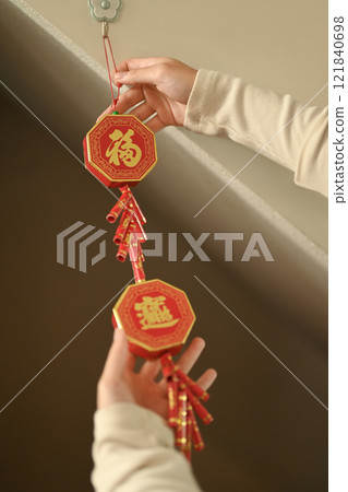 Close up of hands hanging red Chinese New Year decoration adorned with golden Chinese characters for luck and prosperity. Close up of hands hanging red Chinese New Year decoration adorned with golden Chinese characters for luck and prosperity. 121840698