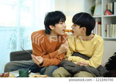 Romantic gay couple enjoys a casual meal together in living room 121840700