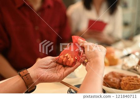 Close up of hands offering a red gift pouch filled with golden treats during a Chinese New Year celebration Close up of hands offering a red gift pouch filled with golden treats during a Chinese New Year celebration 121840711