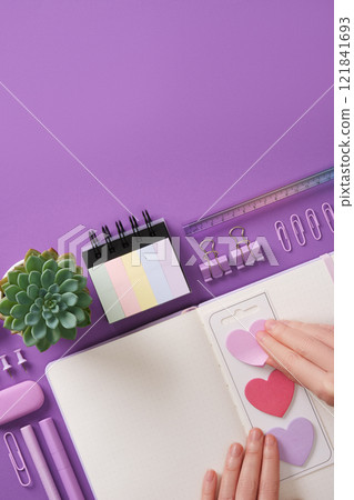 Hand peeling off a heart shaped sticker. Background with purple stationery and heart shaped notes. Place for your text. Hand peeling off a heart shaped sticker. Background with purple stationery and heart shaped notes. Place for your text. 121841693