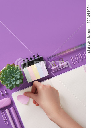Hand applying a heart shaped sticker. Background with purple stationery and heart shaped notes. Place for your text. Hand applying a heart shaped sticker. Background with purple stationery and heart shaped notes. Place for your text. 121841694