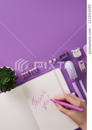 A hand writes the words Thank you in English in a notebook. Against a background of purple stationery and heart shaped notes. A place for your text. 121841695