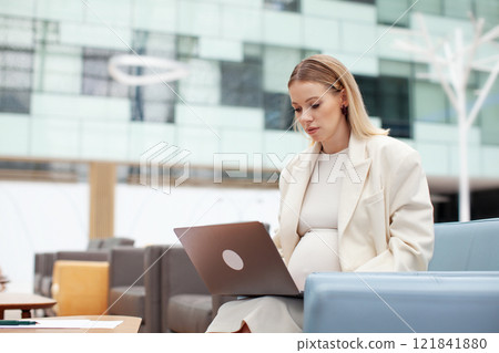 Beautiful pregnant business woman working indoors with a laptop. Pregnant female entrepreneur multitasking in office space, managing business tasks with professionalism and efficiency Beautiful pregnant business woman working indoors with a laptop. Pregnant female entrepreneur multitasking in office space, managing business tasks with professionalism and efficiency 121841880