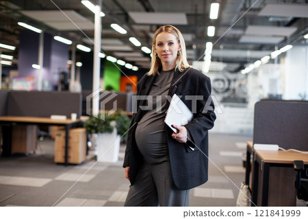 Portrait of a beautiful pregnant woman working in an office with a laptop, showcasing professional and maternity balance in a modern work environment 121841999