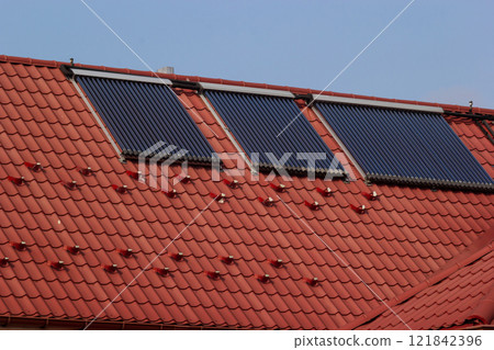 Solar panels on a red tiled roof harnessing renewable energy during daylight in a suburban area 121842396