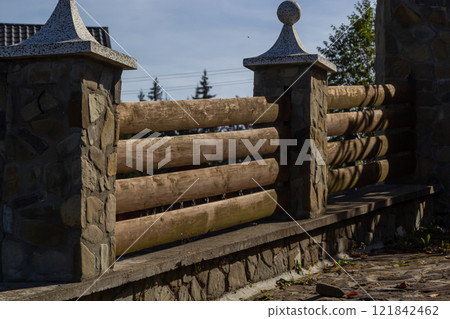 Rustic wooden railing with decorative stone pillars in a sunlit outdoor setting Rustic wooden railing with decorative stone pillars in a sunlit outdoor setting 121842462