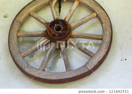 Rustic wooden wagon wheel mounted on a textured wall with a vintage feel and natural colors 121842551