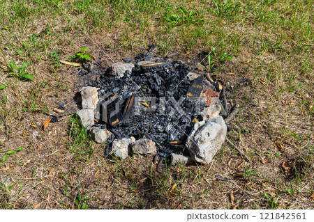 Fire pit remnants after a summer gathering in a grassy outdoor area Fire pit remnants after a summer gathering in a grassy outdoor area 121842561