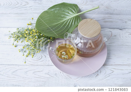Herbal medicinal tea with chamomile flowers in a glass teapot, a bouquet of fresh flowers, on a wooden light background. 121843083