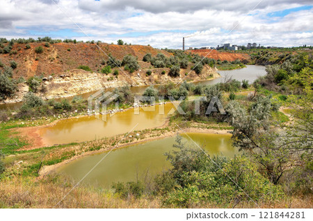 Lush riverbanks with rich vegetation under dramatic cloud patterns by the water's edge 121844281