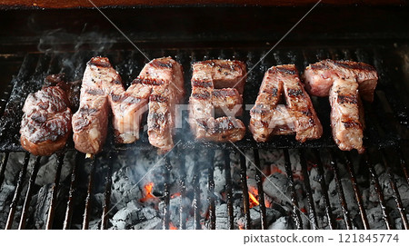 Grilled meat arranged in letters over charcoal flames at a barbecue event 121845774