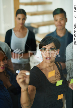 Brainstorming, diverse and creative team writing a strategy idea on sticky notes and creating a schedule on a glass board. Group using teamwork, planning and collaboration in a marketing meeting 121845890
