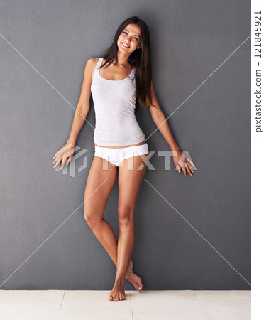 Healthy, fit and beautiful young woman posing in underwear against a grey background in studio. Attractive, stunning and seductive female feeling carefree and standing in a tank top and panties 121845921