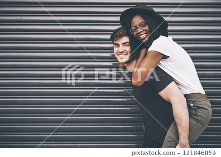 Cute, loving and affectionate interracial couple having fun, being playful and enjoying time together on copy space background. Happy boyfriend giving young girlfriend a piggyback ride outside 121846059