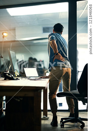 Putting his health at risk for the sake of business. Rearview shot of a businessman suffering from backache while working at night. Putting his health at risk for the sake of business. Rearview shot of a businessman suffering from backache while working at night. 121846068