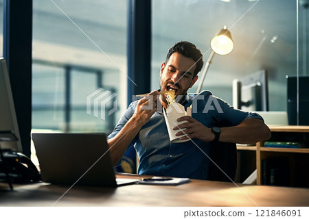 Young hungry businessman working late and eating at desk. Man having takeout food in the office at work station in the evening. Male entrepreneur eating asian meal during the night at the workplace 121846091