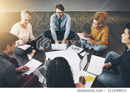 Group of business people talking, planning with documents and sitting in a meeting on floor in an office together at work. Diverse, happy and smiling casual workers writing notes and browsing on tech 121846631