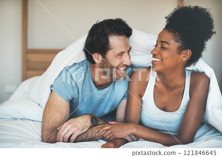 Happy, carefree and laughing couple having fun lying in bed together. Interracial husband and wife bonding and showing affection while talking. Smiling lovers enjoying time indoors being playful 121846645