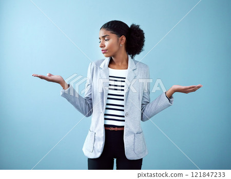 Professional black corporate business woman making a hand gesture for decision, choice and balance while standing against a blue studio background alone. One African manager choosing between ideas 121847233