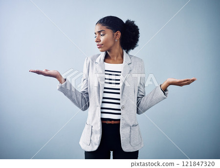 Female thinking about a business option or choice for a decision between offers. Confused, anxious female shrugging, doing balance hand gesture with a grey copyspace background. 121847320