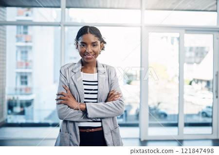 Confident, proud and professional young black business woman folding her arms and smiling in a modern office. Portrait of African American leader looking powerful, successful standing in power stance Confident, proud and professional young black business woman folding her arms and smiling in a modern office. Portrait of African American leader looking powerful, successful standing in power stance 121847498