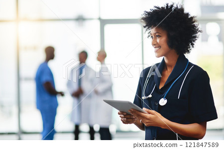 Young smiling medical professional doctor, holding digital tablet in modern hospital. Female healthcare specialist standing with test results, with colleagues in background. Young smiling medical professional doctor, holding digital tablet in modern hospital. Female healthcare specialist standing with test results, with colleagues in background. 121847589