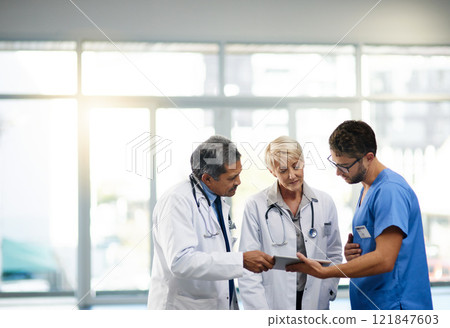 Team or group of doctors, nurses and medical professional talking, meeting and discussing healthcare in a hospital. Health practitioners in labcoats looking at records on a tablet in a clinic 121847603