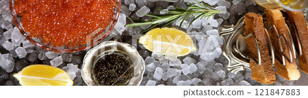 Natural black and red caviar on table. Caviar in transparent dish lies on ice. Ice is scattered on table. Natural omega. Top view. Narrow banner for advertising. 121847883