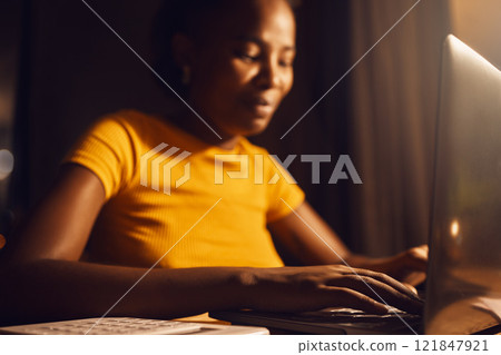 Woman freelancer working remote on a laptop while typing and answering emails online. Smiling, positive black female entrepreneur completing a project late at night while sitting at a desk at home Woman freelancer working remote on a laptop while typing and answering emails online. Smiling, positive black female entrepreneur completing a project late at night while sitting at a desk at home 121847921