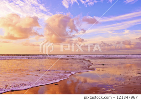 Beautiful beach and fresh ocean against a soft cloudy sky at sunset with copy space. Waves washing onto a shore on a relaxing, scenic coast. Golden sun shining on fluffy clouds on a fresh morning 121847967