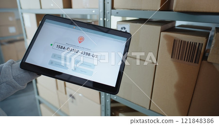 Postal Warehouse Associate Scans Code on Cardboard Box, Checks Parcel Information on Tablet 121848386
