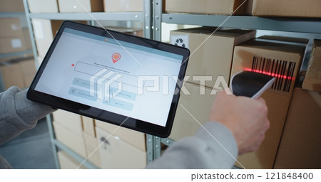 Postal Warehouse Associate Scans Code on Cardboard Box, Checks Parcel Information on Tablet 121848400