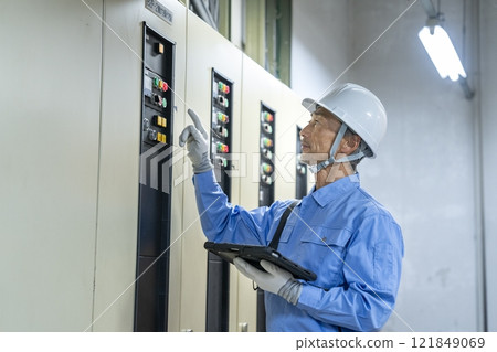 Image of a worker inspecting the building's electrical equipment with a tablet, building maintenance staff Image of a worker inspecting the building's electrical equipment with a tablet, building maintenance staff 121849069