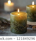 Green decorative candle with natural botanical design, lit and placed on a rustic wooden surface. Studio photography. Cozy home decor and relaxation concept for design and interior inspiration 121849296