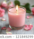 Pink candle in a glass jar surrounded by rose petals on a wooden surface. Romantic composition with a soft-focus background 121849299