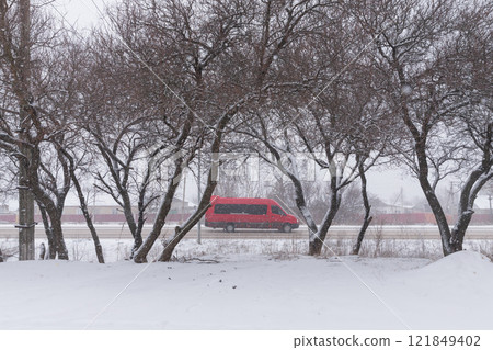 [Ukraine] Snowfall, street trees and a red van driving along the road in the eastern Donbas region 121849402
