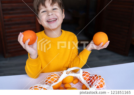 A child with a joyful smile holds an orange and a mandarin, looking at the camera. 121851165