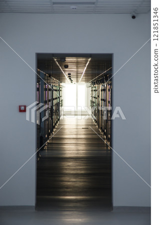 Modern corridor with server racks and bright window at the end. Perspective interior view of a technology facility. Data center infrastructure. Vertical photo for design and print Modern corridor with server racks and bright window at the end. Perspective interior view of a technology facility. Data center infrastructure. Vertical photo for design and print 121851346