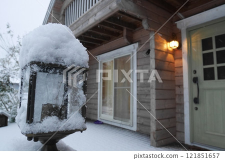 入口處亮著燈的木屋，戶外燈被雪覆蓋 121851657