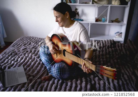 a senior woman learns to play the guitar with online lessons 121852568