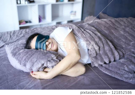 a senior woman in silk eye mask sleeping under heavy blanket 121852586