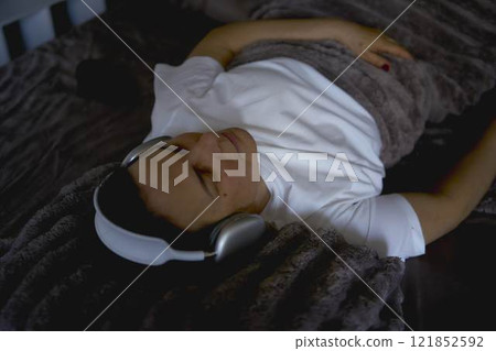 a senior woman wearing sonic hues sleep headphones sleeping under a weighted blanket 121852592